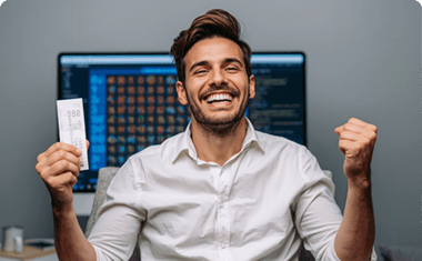 Muž s výherním tiketem v ruce a radostným výrazem sedící před monitorem.
